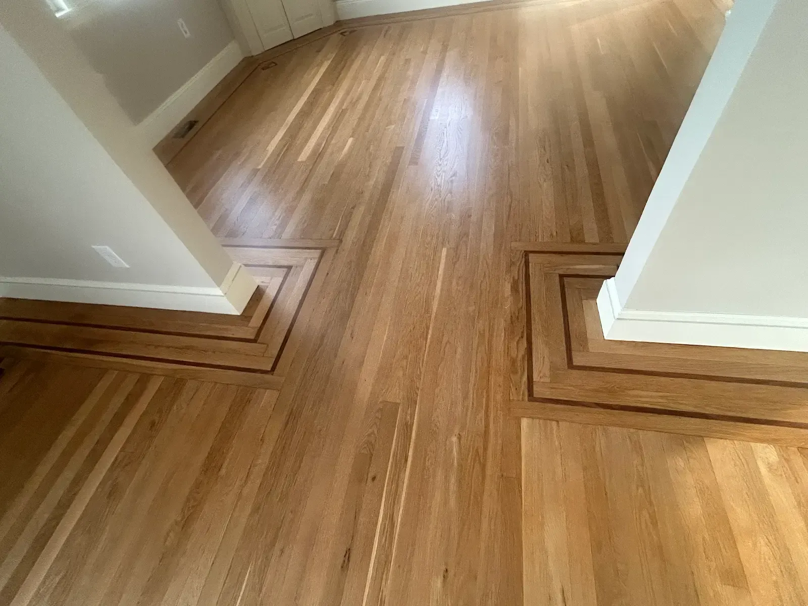 Wooden hallway floor with decorative square trim around two doorway bases and white walls.