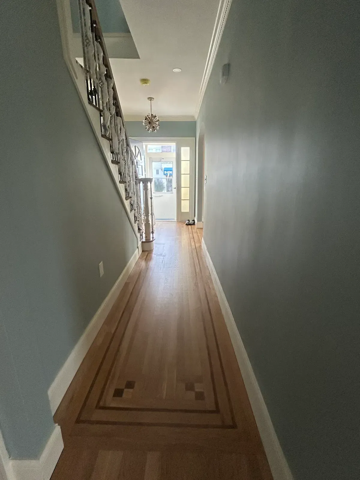 Narrow hallway with wood floors, gray walls, and a bright doorway at the end.