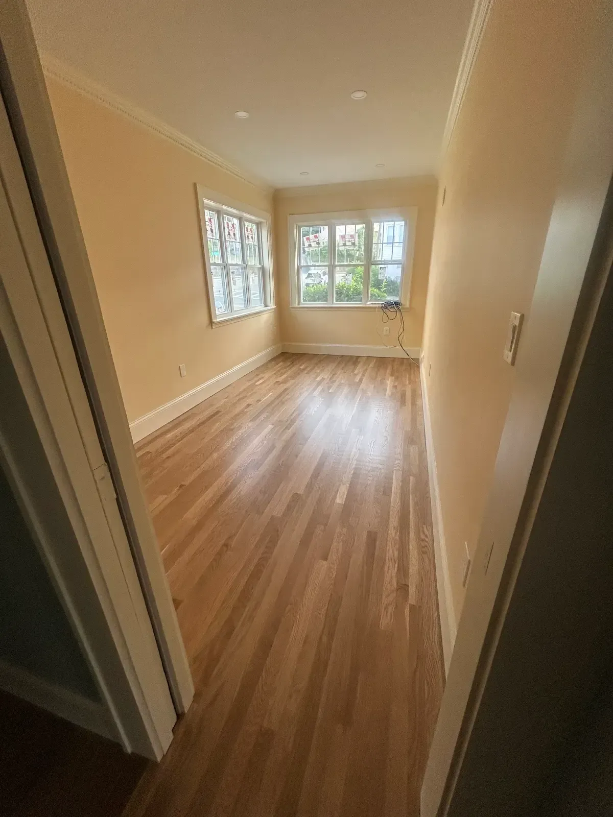 Empty sunlit room with hardwood floors and large windows