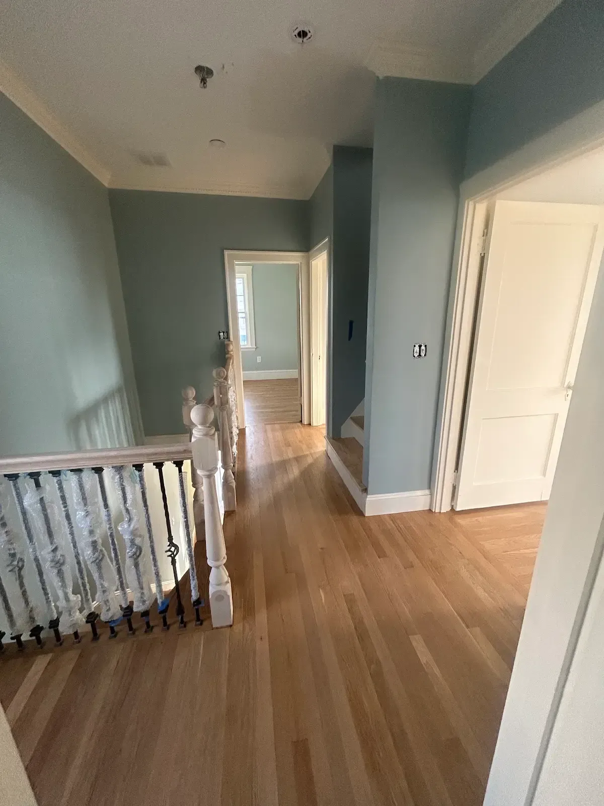 Empty hallway with light wood floors, blue-gray walls, and a white railing overlooking stairs.