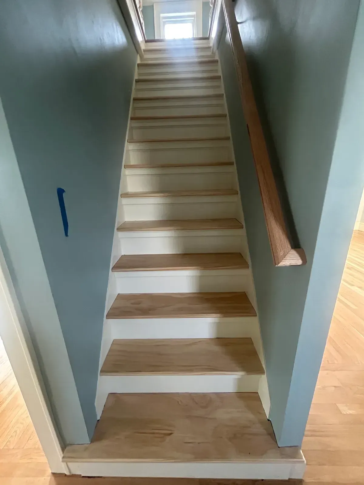Narrow indoor staircase with white steps, wood handrail, and light blue walls, viewed from the bottom