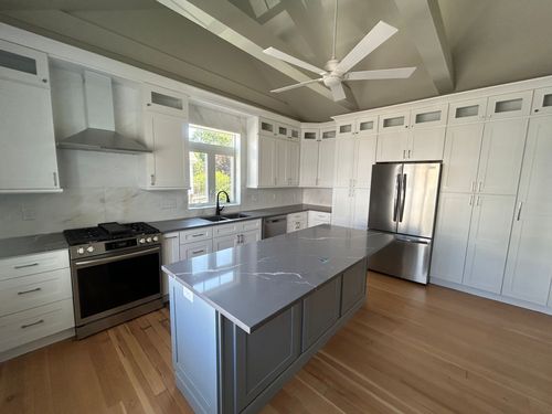 Bright modern kitchen with white cabinets, gray island, stainless appliances, and wood floors