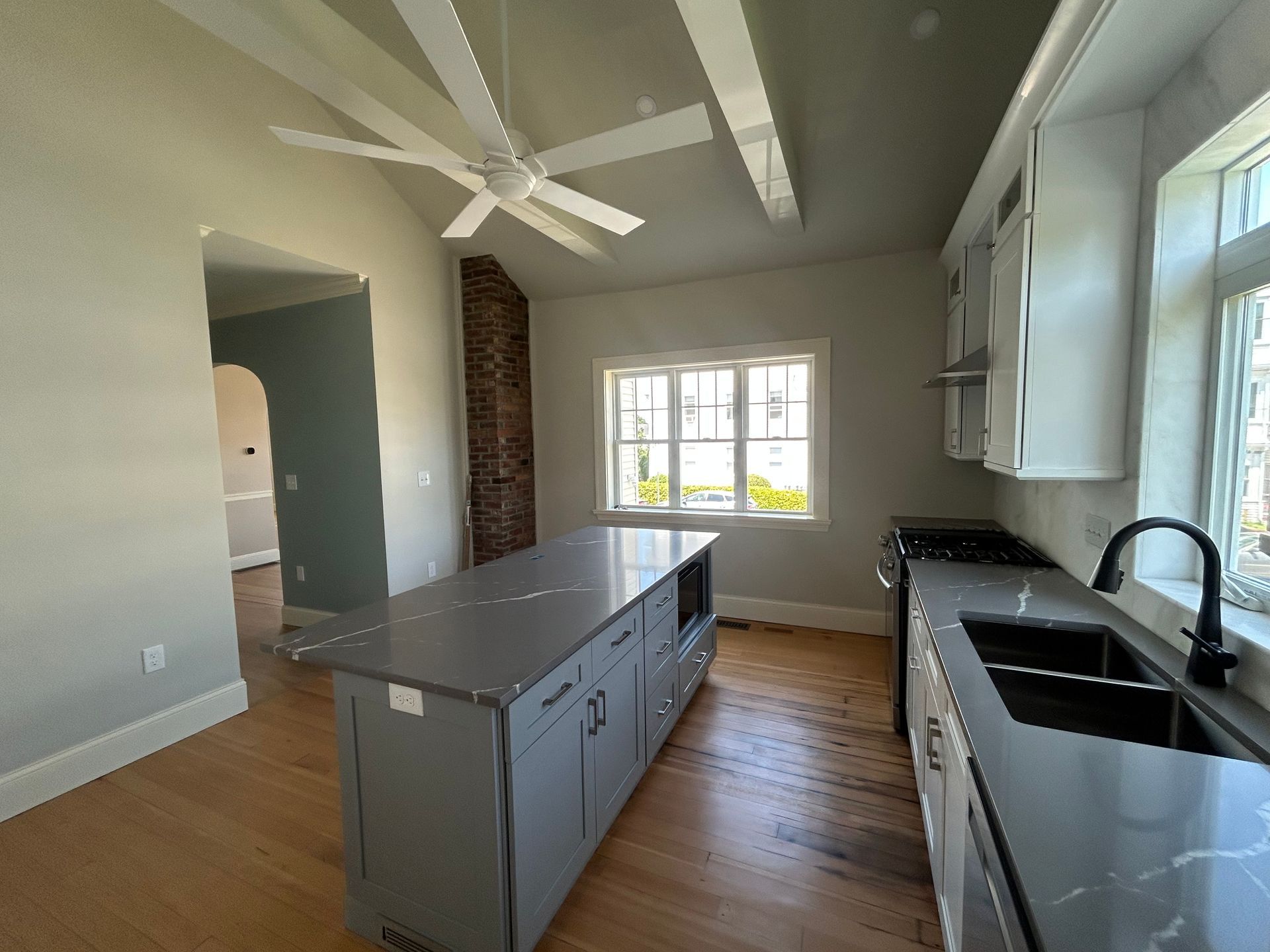 Bright modern kitchen with gray island, black sink, white cabinets, and ceiling fans near a window.