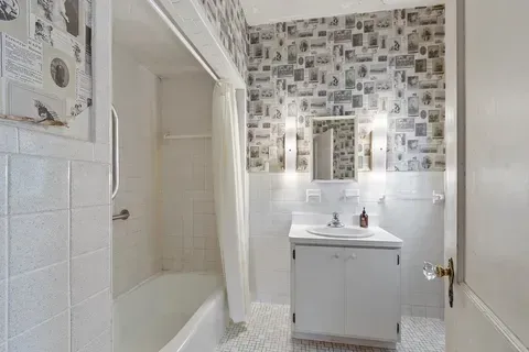 Small bathroom with tub, white vanity, and photo-print wallpaper