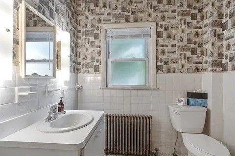 Small bathroom with patterned wallpaper, white sink, toilet, frosted window, and radiator.
