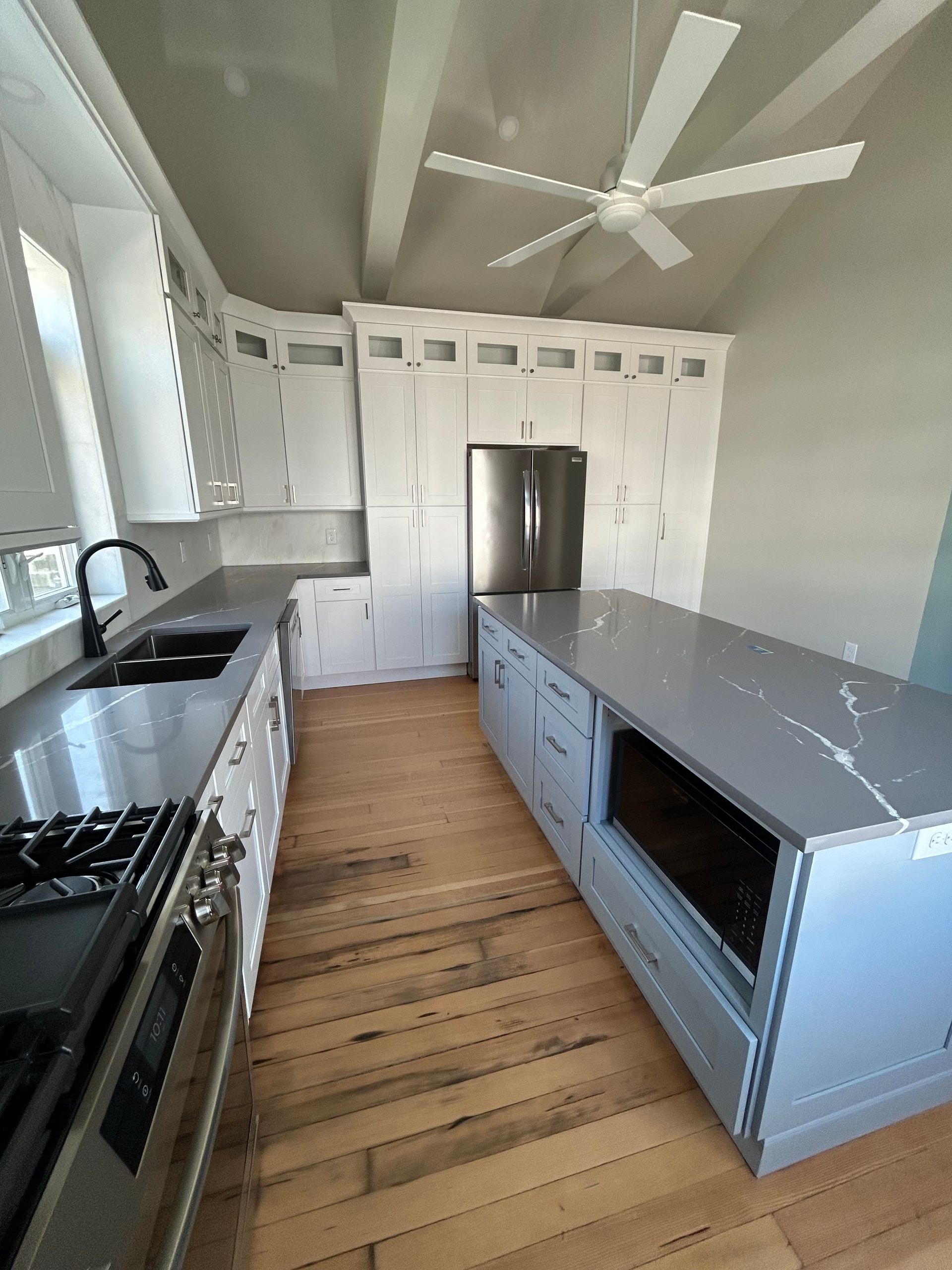 Modern galley kitchen with white cabinets, stainless steel appliances, and a long gray island with seating.
