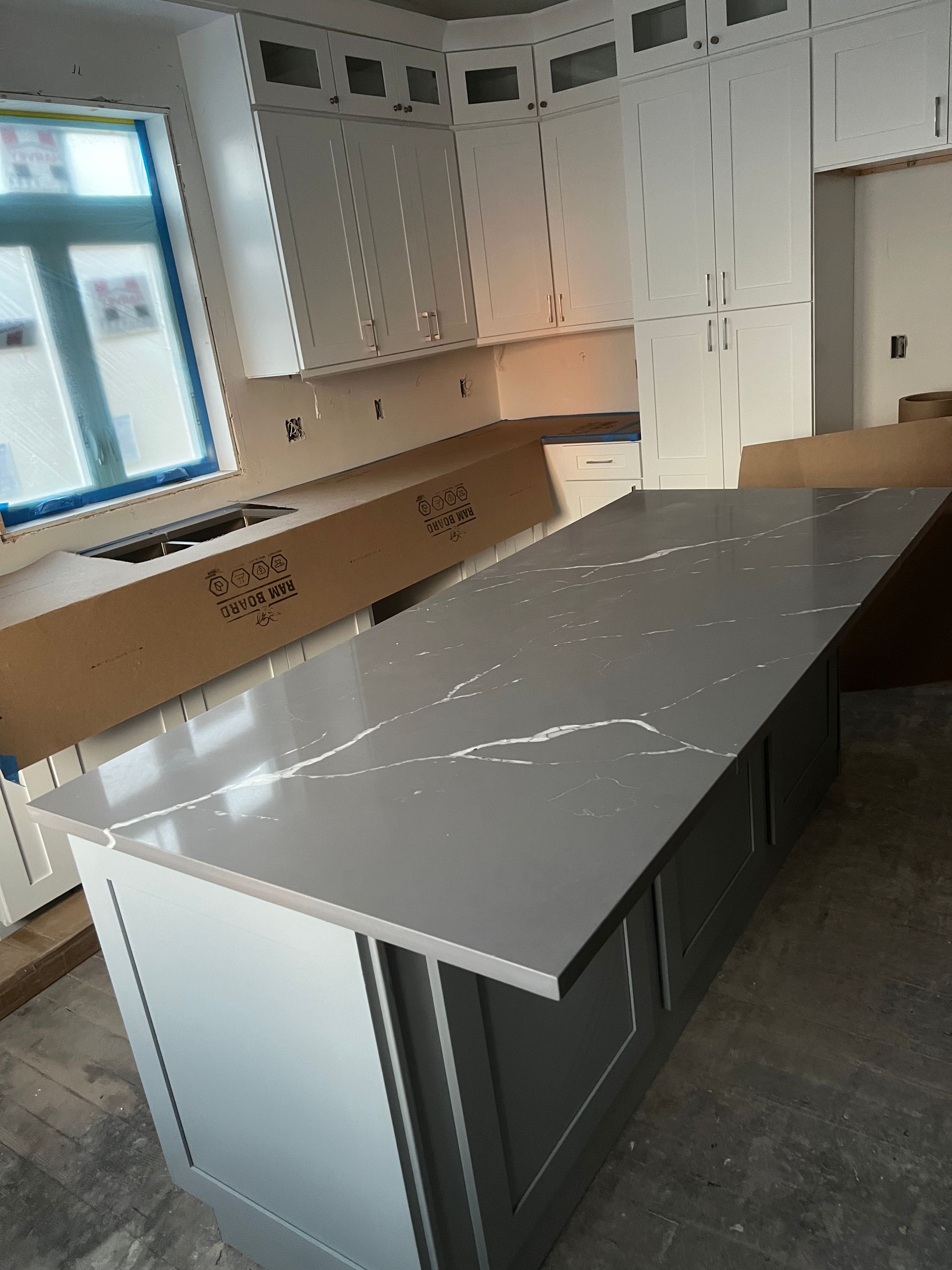 Empty modern kitchen with gray island, white cabinets, and large windows.