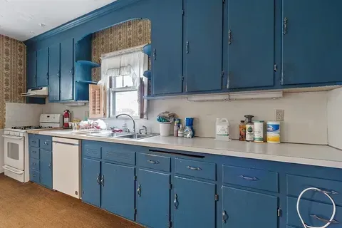 Blue kitchen with white countertops, sink, window, and cabinets lining the wall