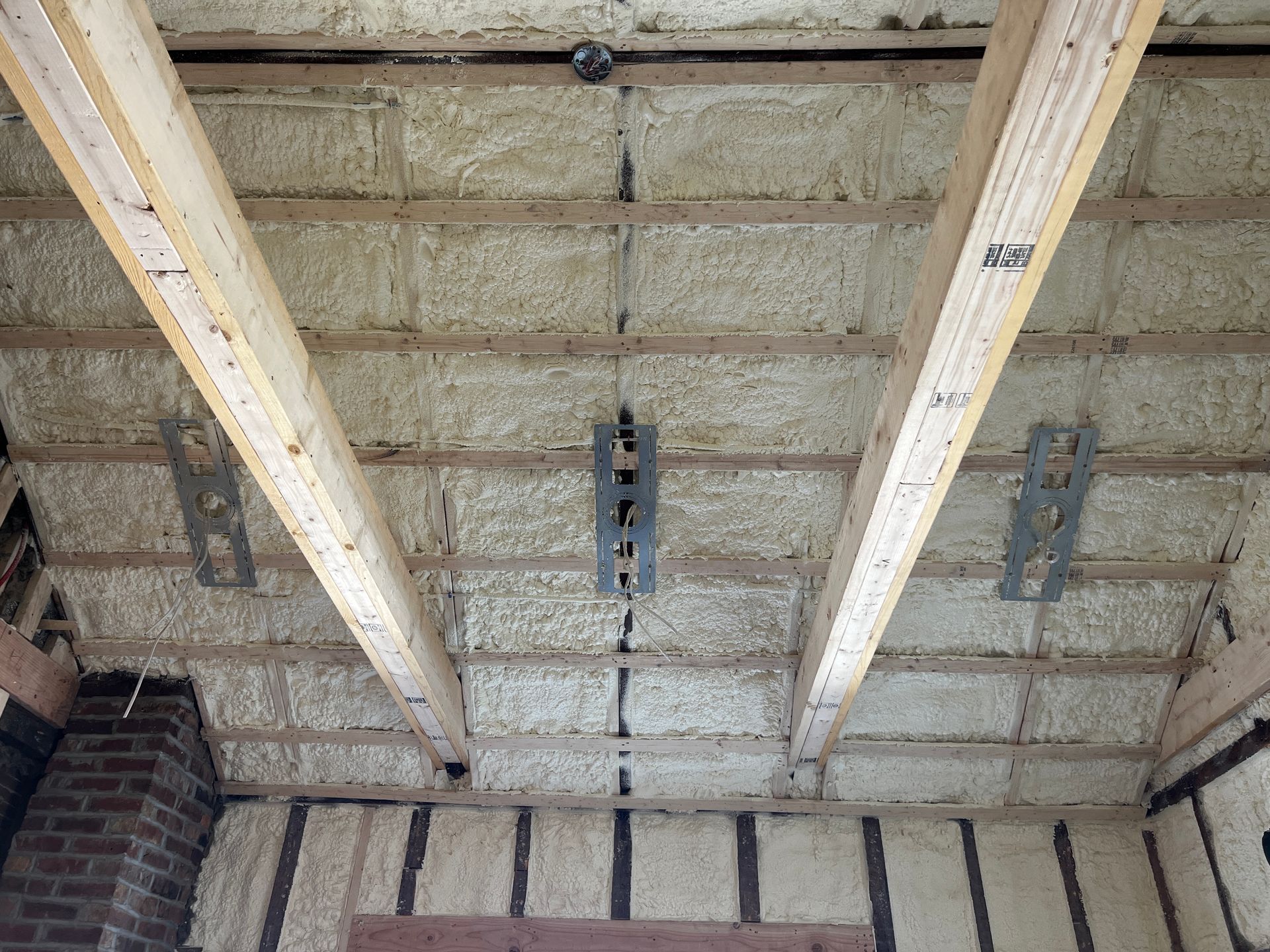Ceiling insulation between exposed wooden beams and brick walls in an unfinished room