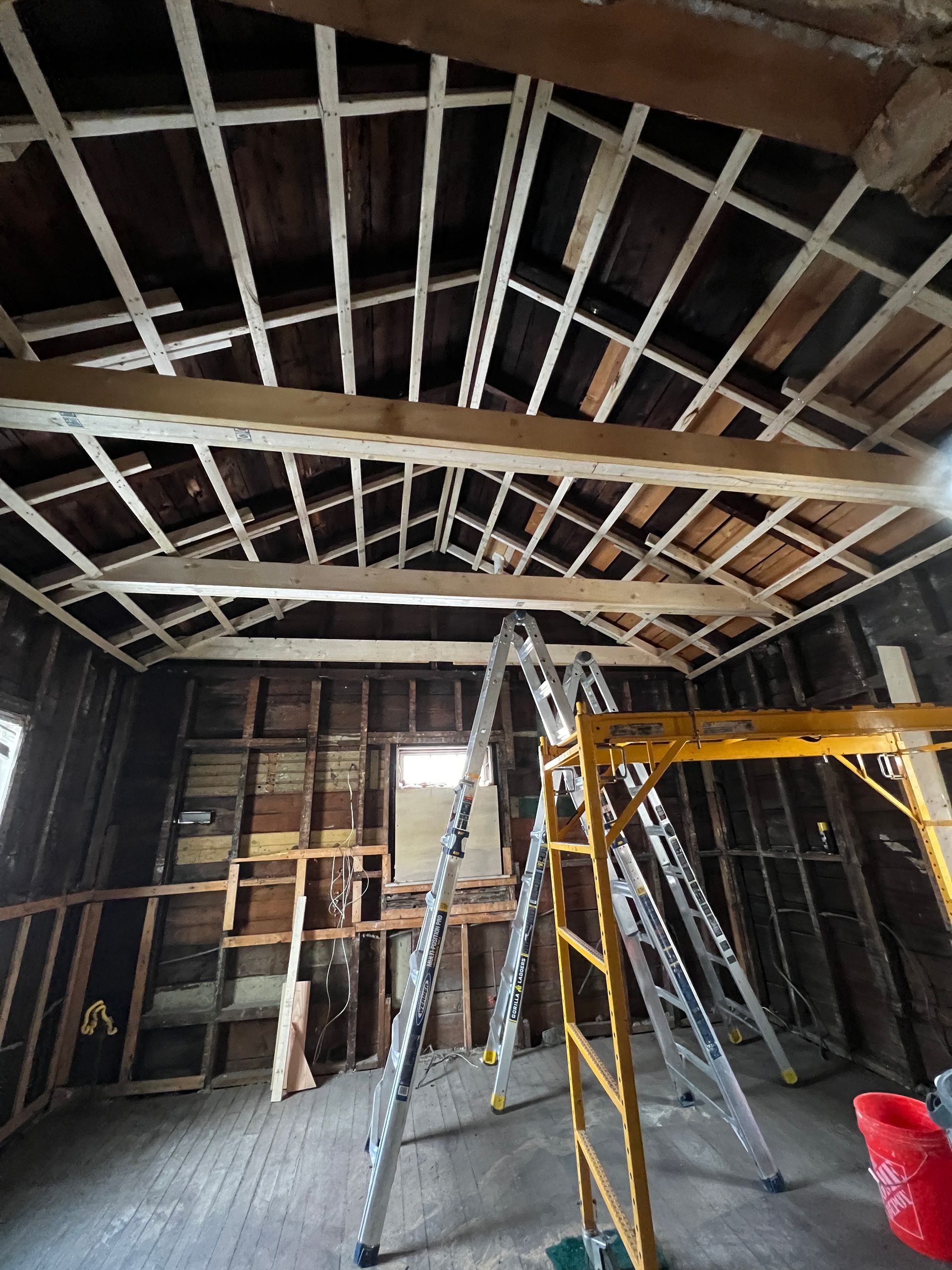 Construction site interior with exposed beams, ladders, and tools in an unfinished room