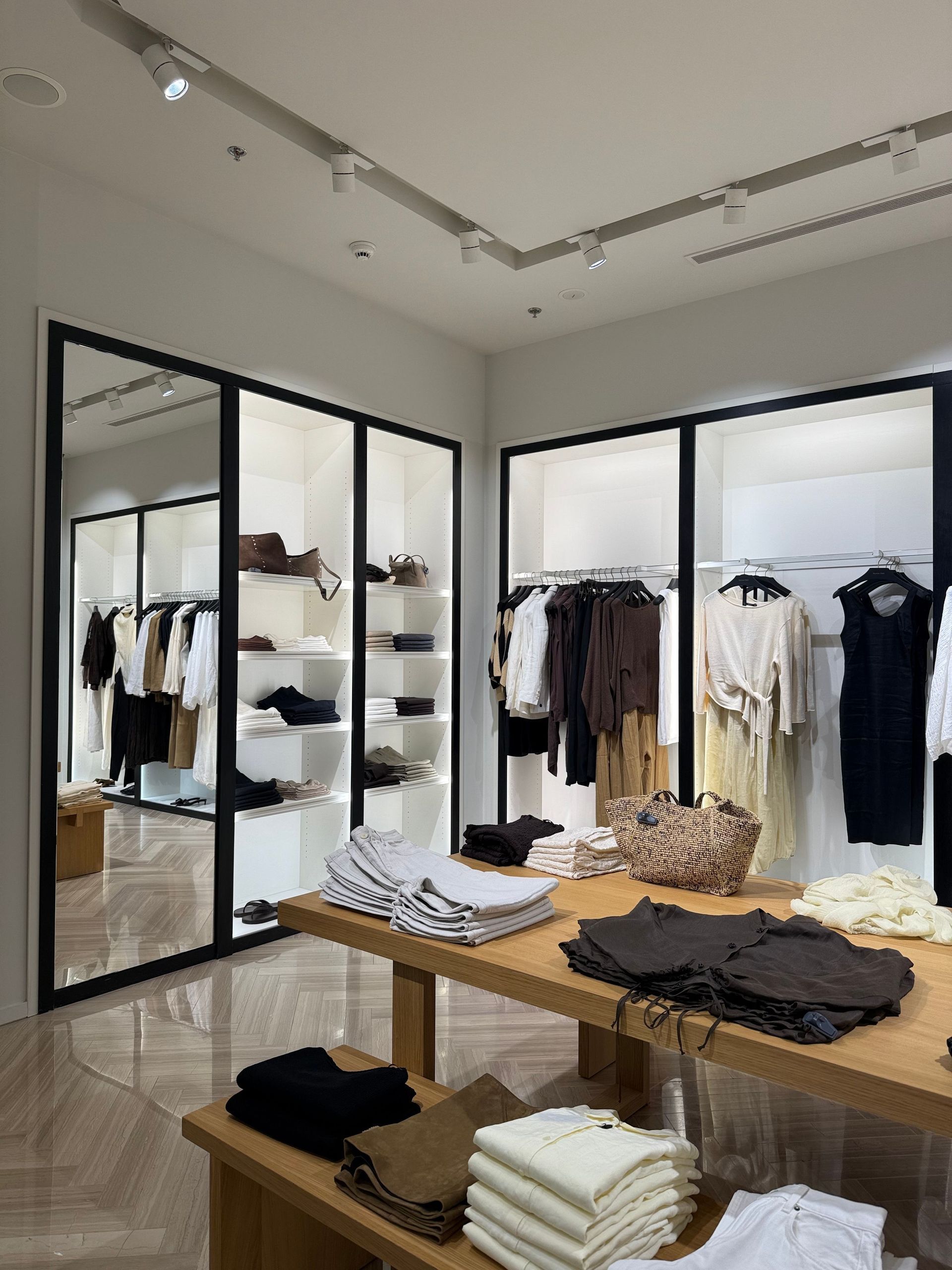Modern clothing store interior with racks of neutral-toned clothes and folded garments on a wooden table
