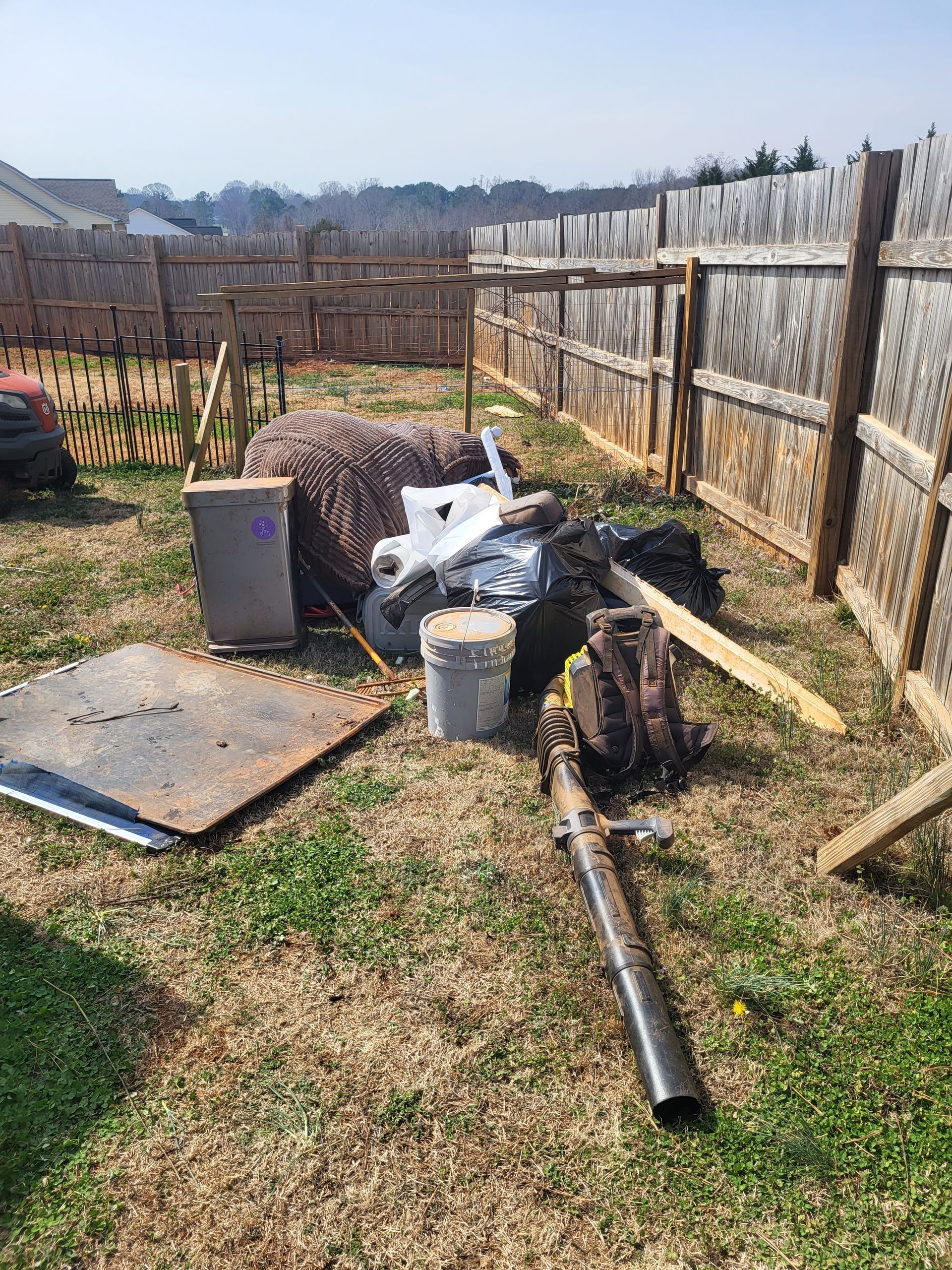 Backyard with a garden fence, scattered tools, and a black pipe on the ground