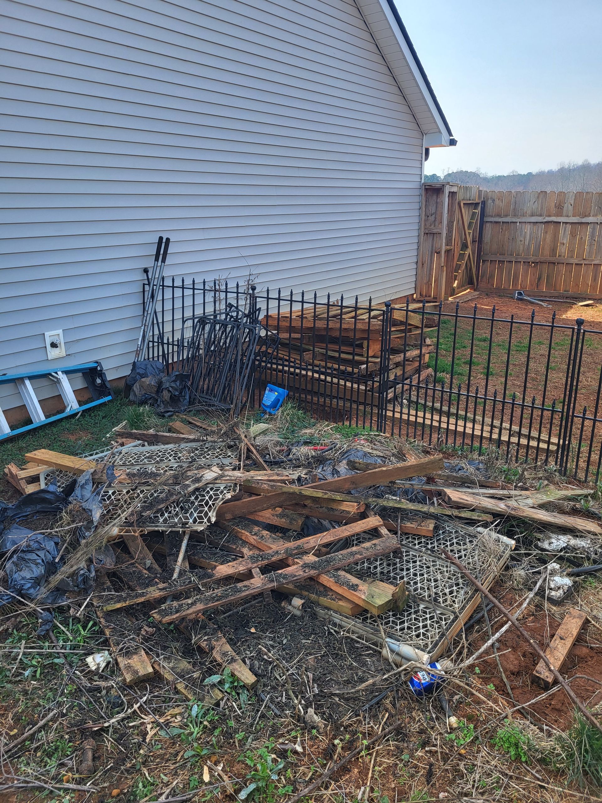 Backyard with scattered scrap wood and metal fencing beside a white house in muddy ground