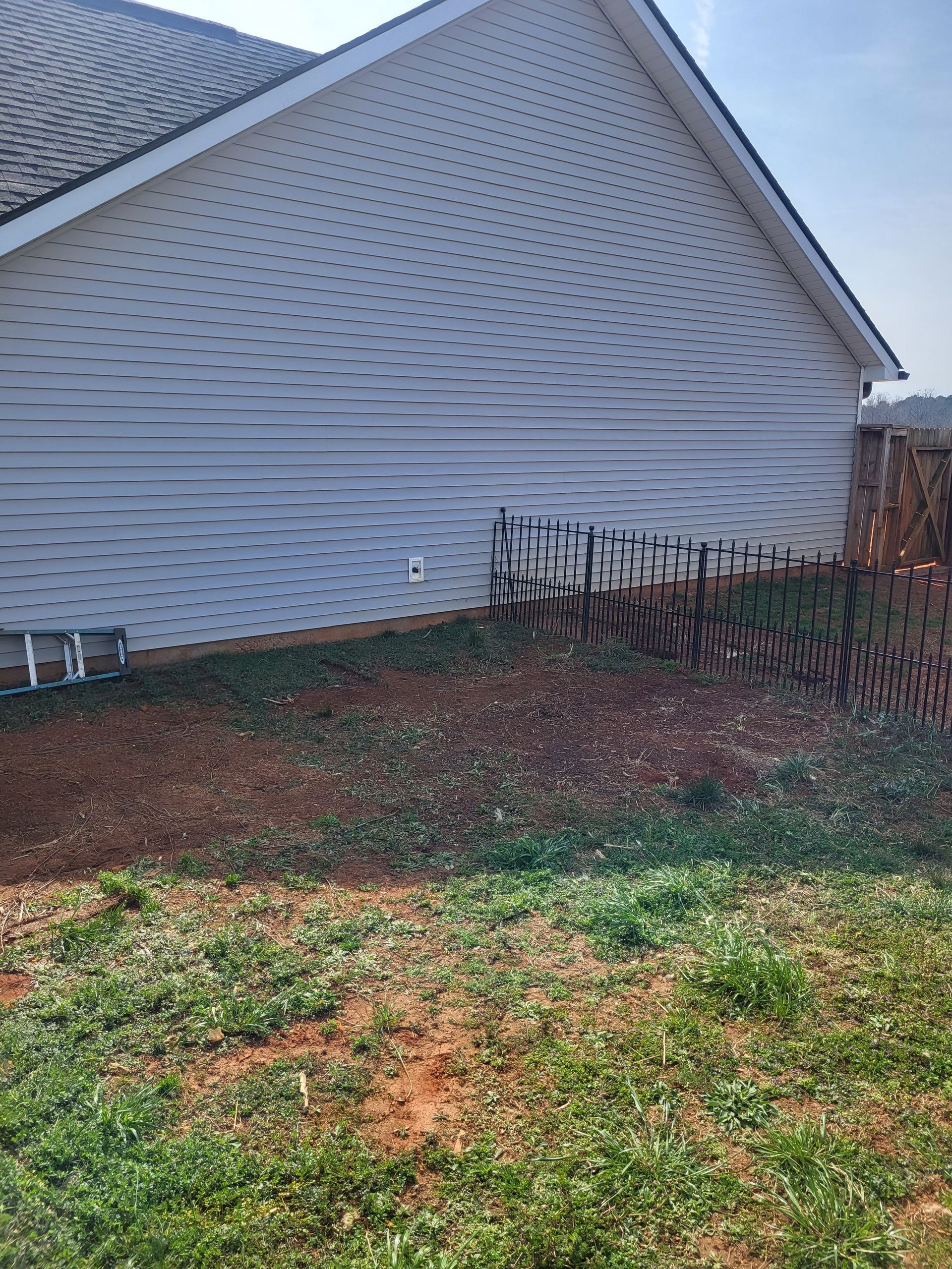 Side view of a house with light siding, a small yard, and a garden bed with bare shrubs