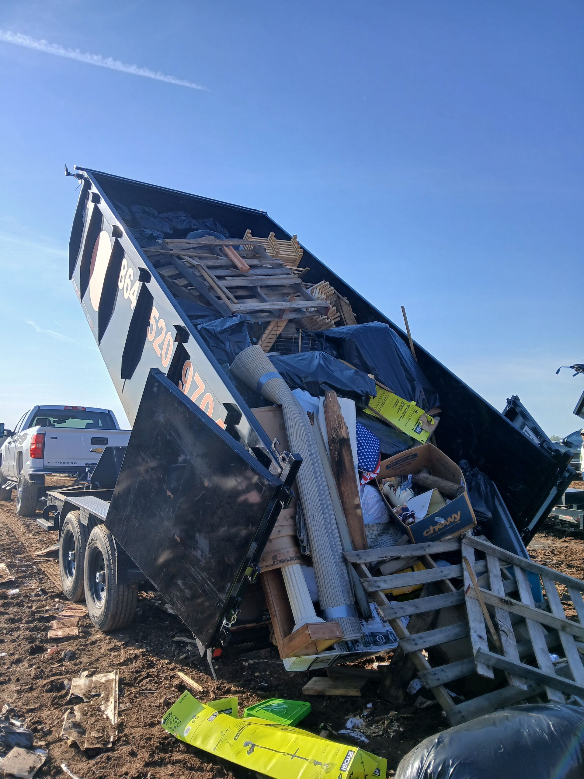 Damaged dump truck tipped on its side in a rocky roadside area under a clear blue sky