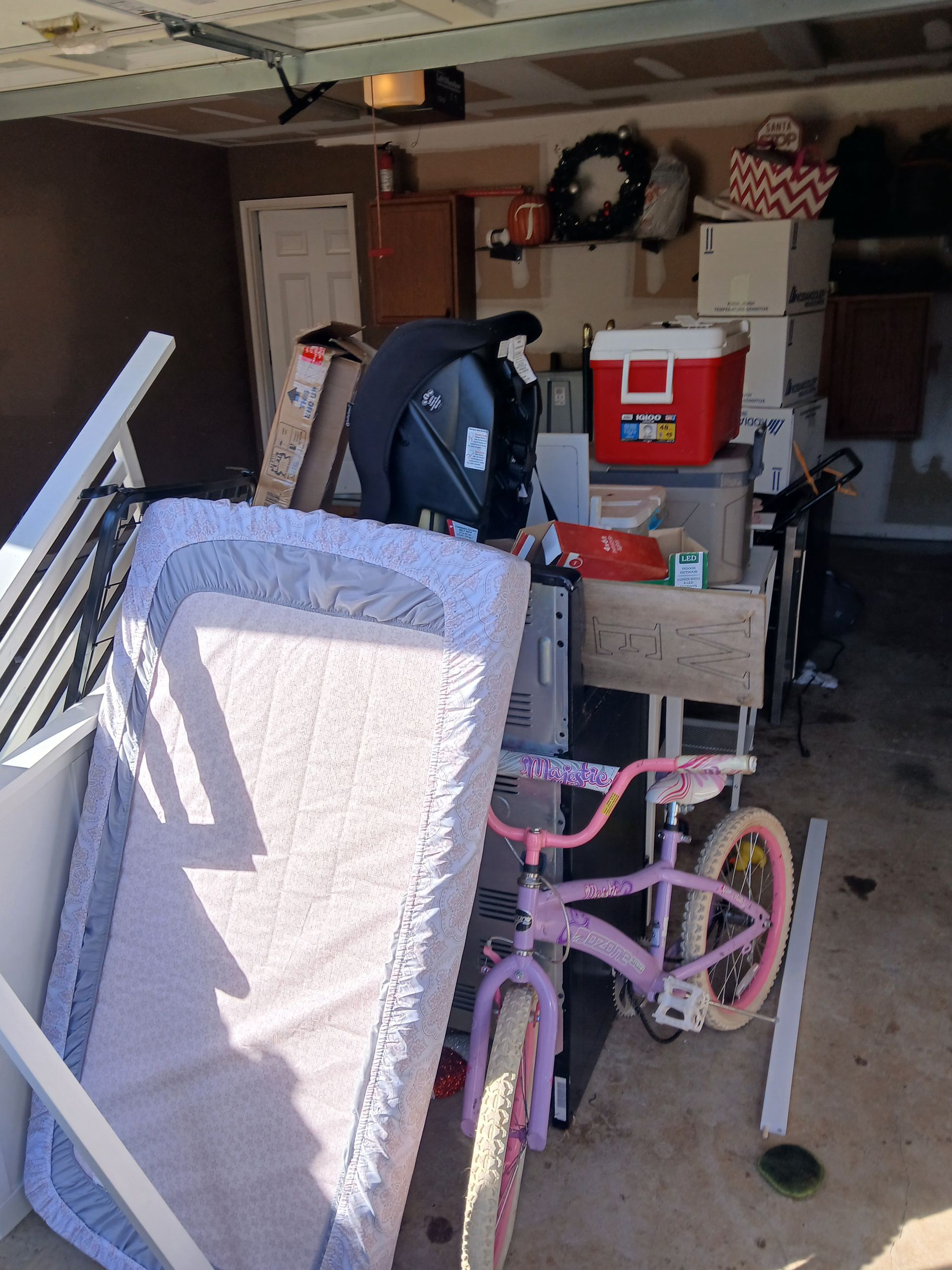 Garage clutter with a person sorting items beside a pink bicycle and a mattress leaning against the wall