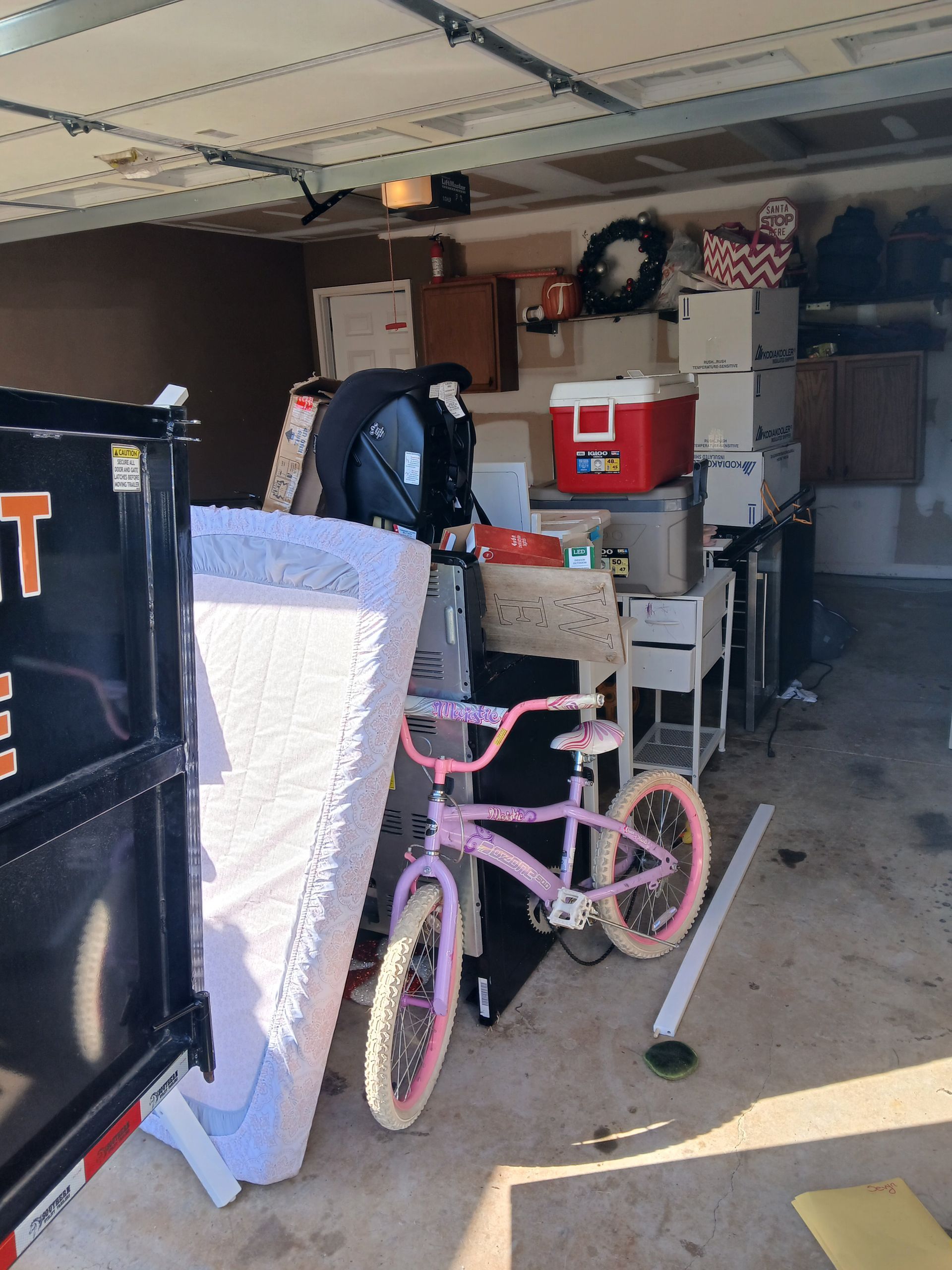 Cluttered garage packed with storage boxes, a pink bicycle, and shelves under an open garage door