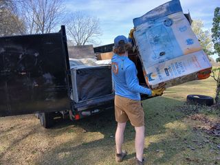 Person loading a large cardboard box into a black truck in a grassy yard