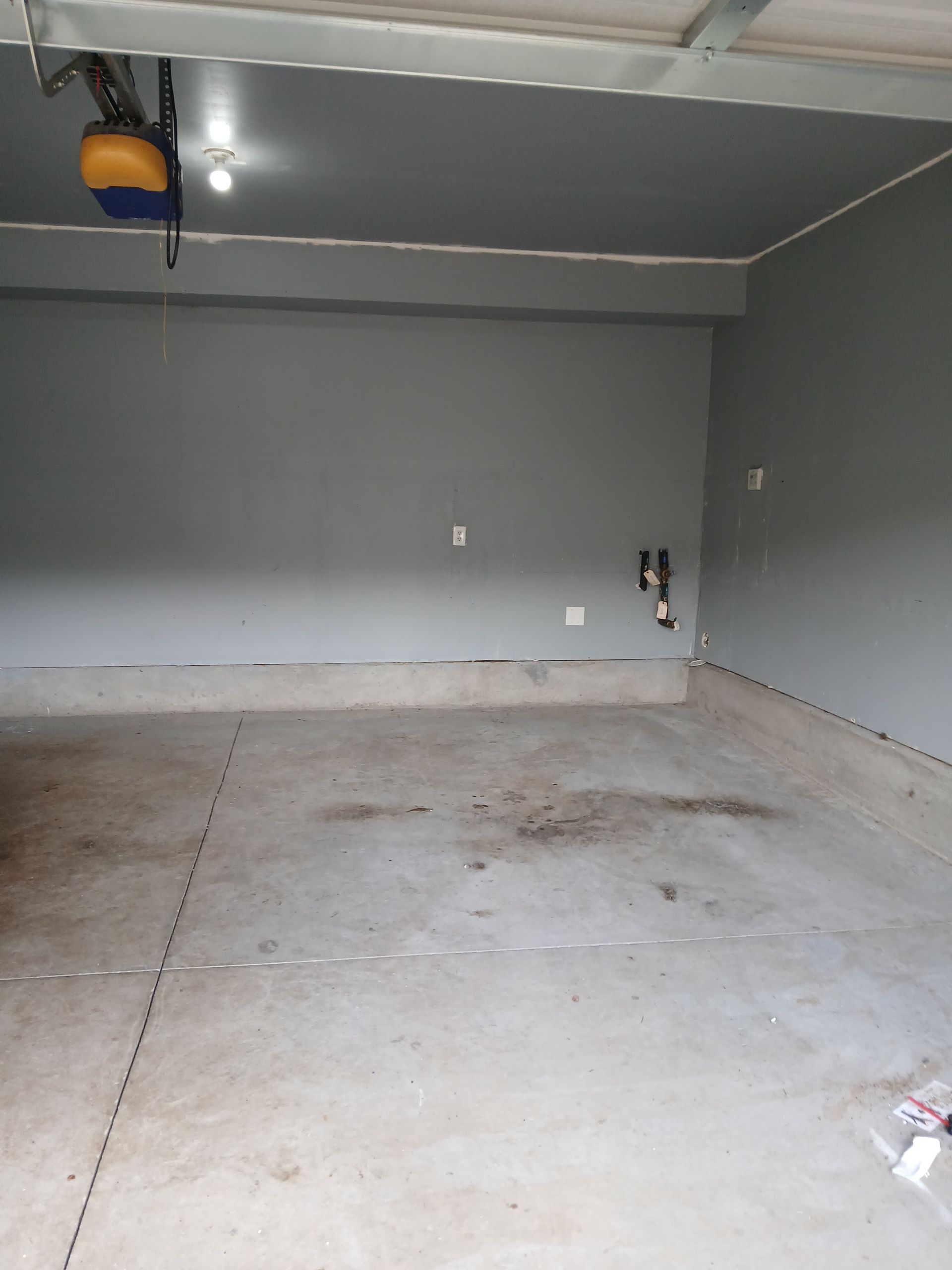 Empty gray garage with a concrete floor and closed overhead door opener.