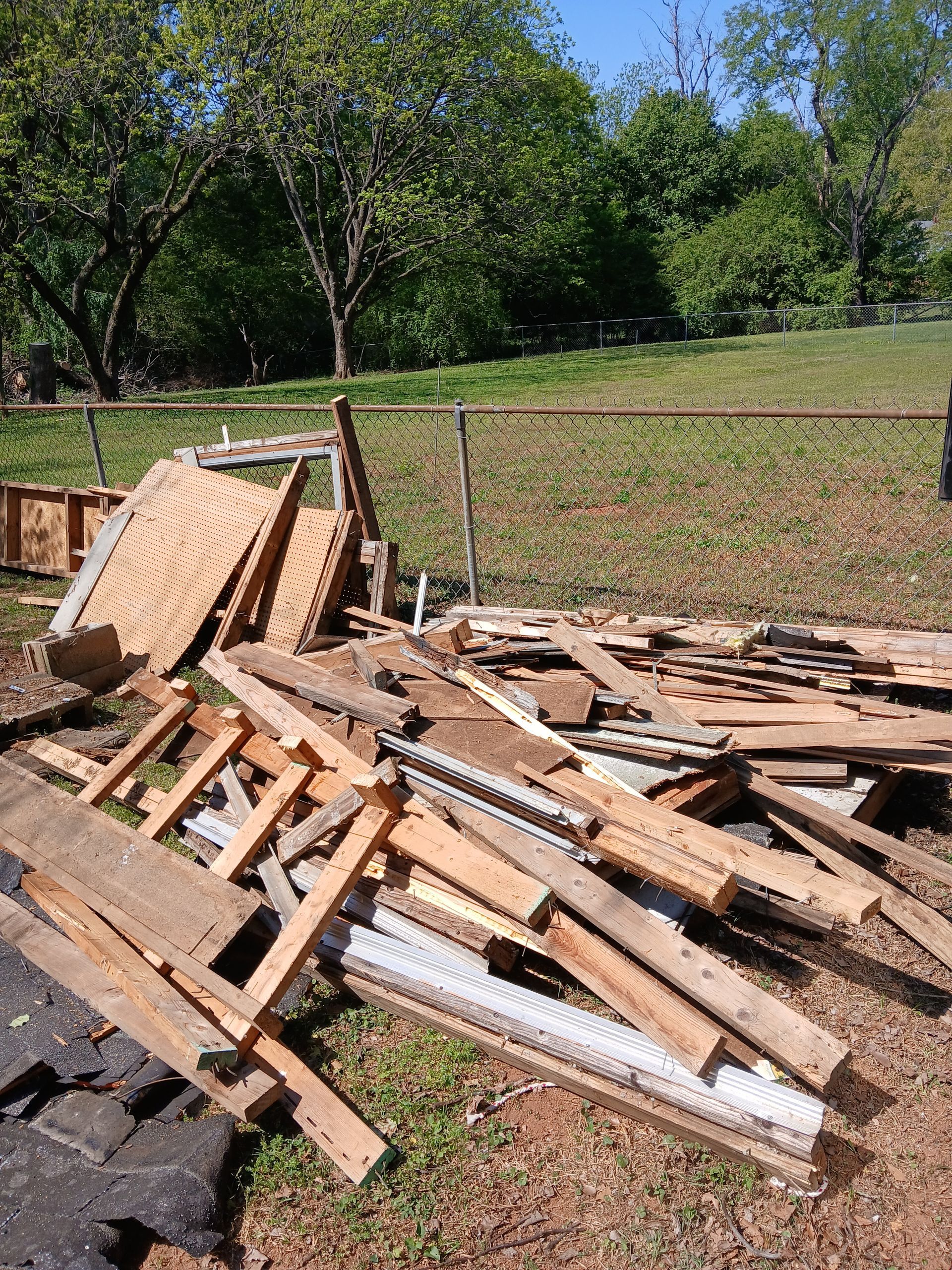 Pile of broken wooden pallets and debris on grass beside a road in a rural area.