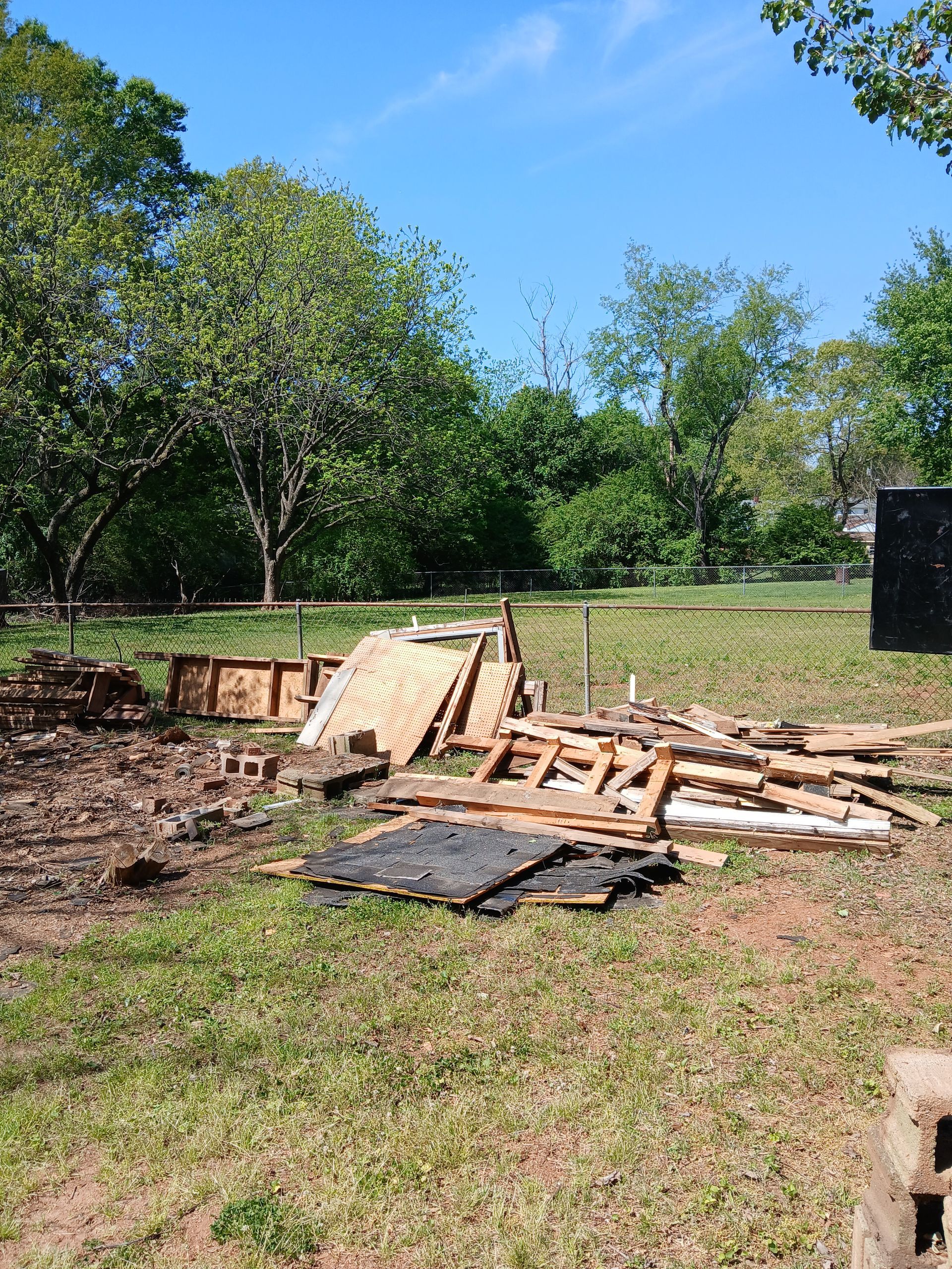 Debris and broken wooden pallets scattered on grass beside trees under a blue sky