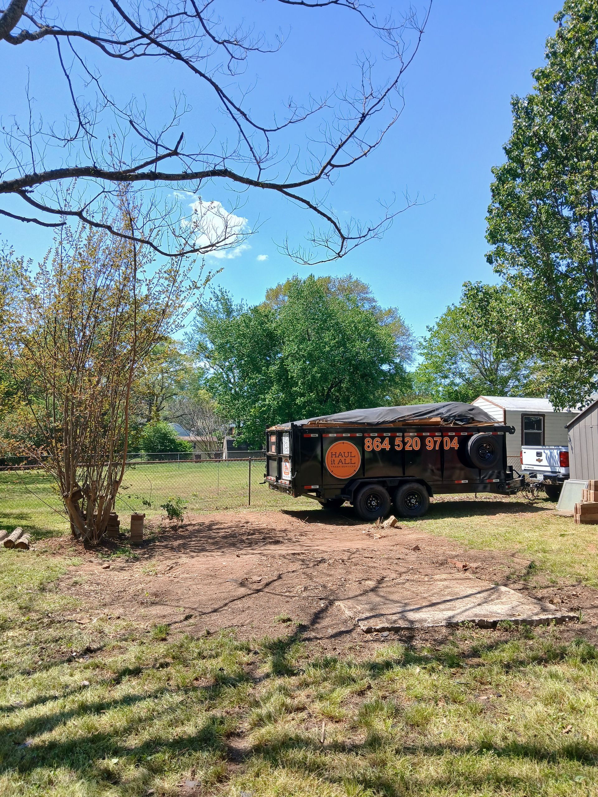 Black food truck parked in a grassy yard under blue sky with trees around it.