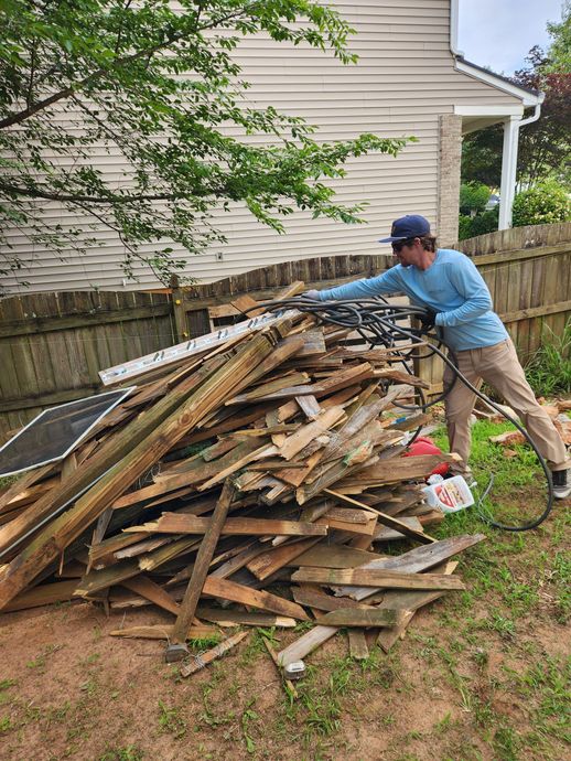Person in blue shirt pushing a large pile of scrap wood in a backyard beside a house.