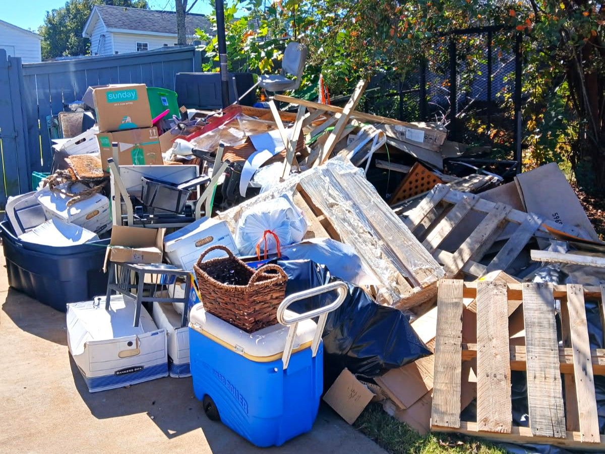 Overflowing pile of construction debris, pallets, and household junk in a sunlit outdoor yard