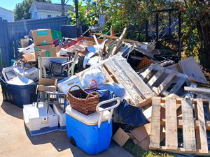 Outdoor pile of discarded furniture, boxes, and wooden pallets in a yard or alley