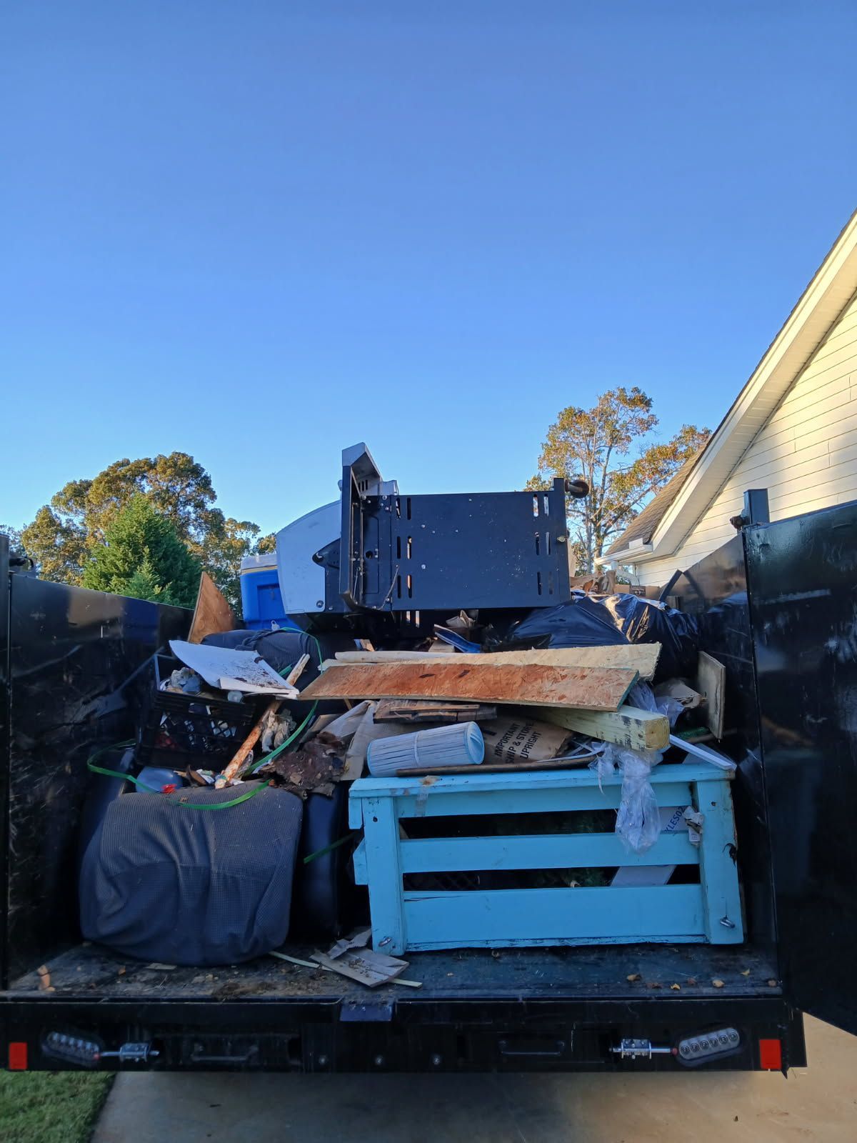 Pickup truck bed piled high with scrap wood, metal, and debris against a blue sky.