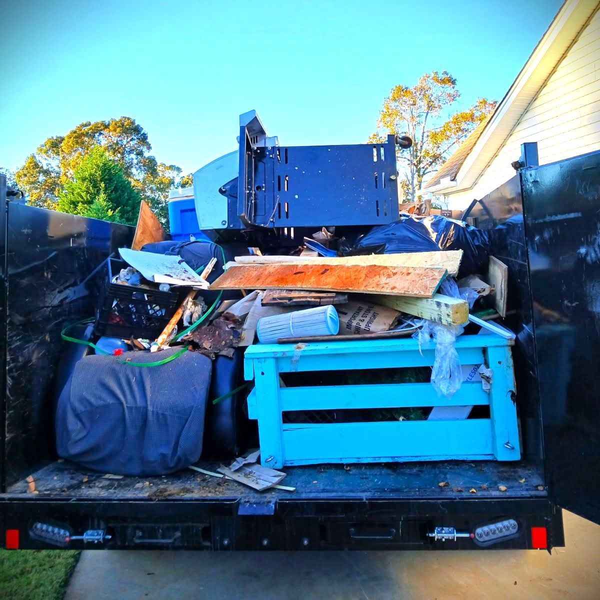A pickup truck bed piled high with mixed junk and debris, including a blue cabinet and wood scraps.