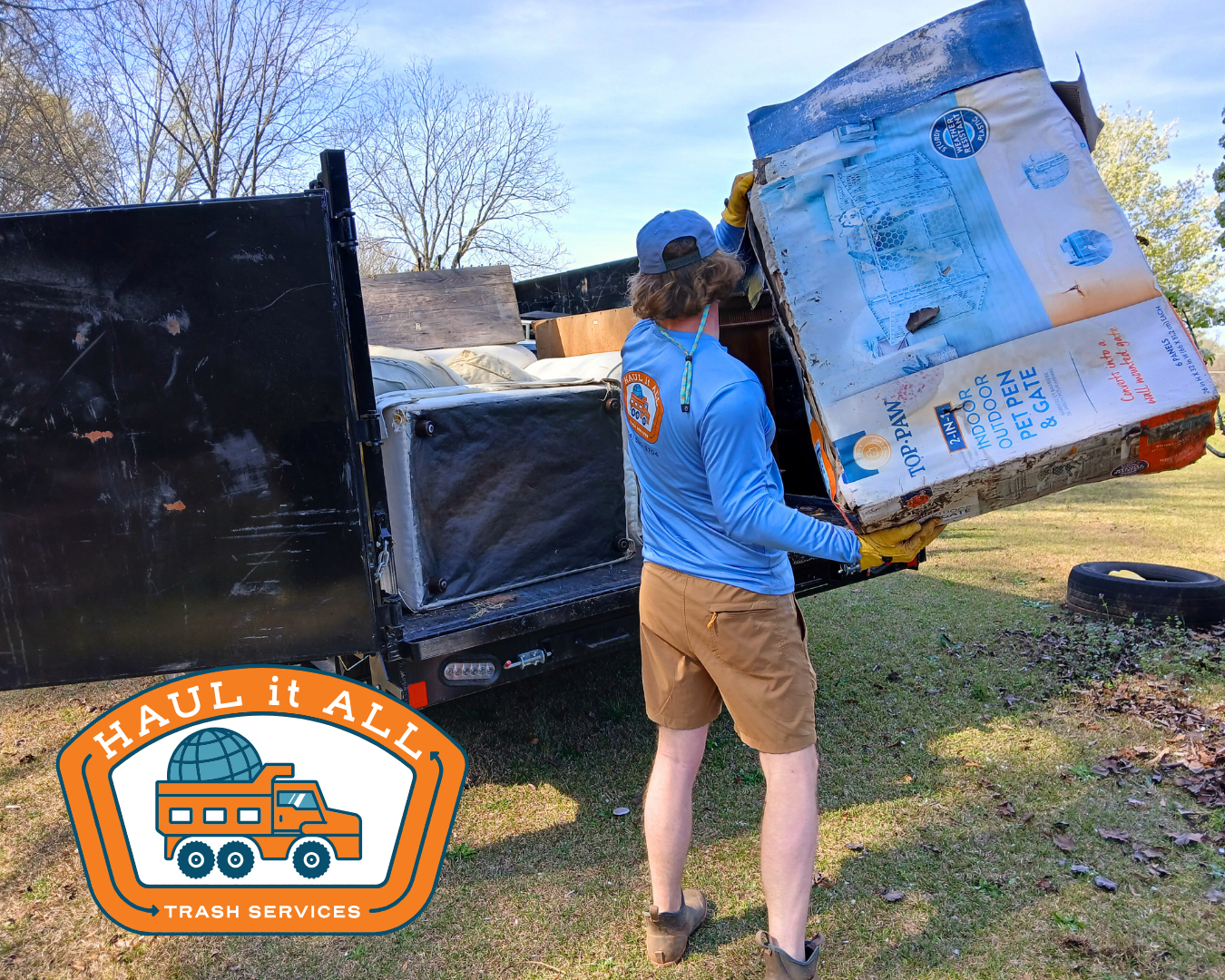 Person carrying a large box near a moving truck in a yard; U-Haul It All logo in corner