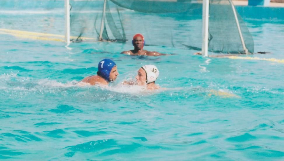 Water polo match: Two players in the water near the goal; goalie watches.