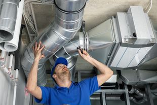 Technician inspecting silver HVAC ducts in a ceiling space