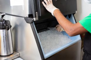 Worker in a green shirt and gloves operating an industrial ice-making machine.