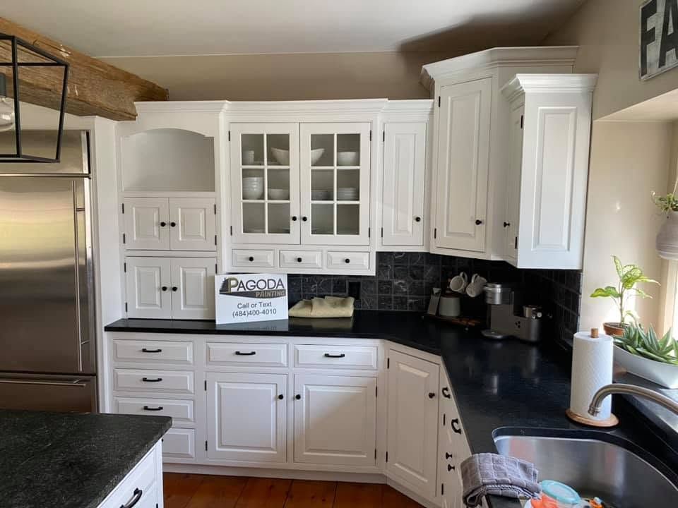 Bright white kitchen with black countertops, stainless refrigerator, and sink by a window.