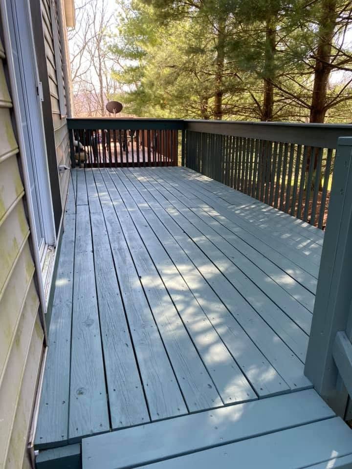 Empty blue-gray wooden deck with railing, surrounded by trees in dappled sunlight.