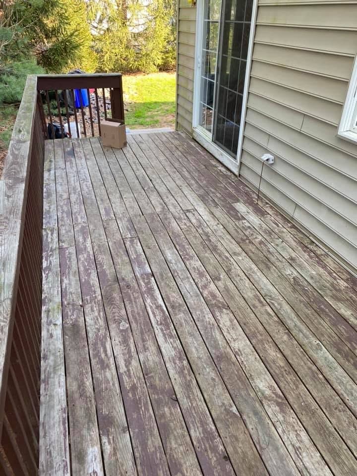 Weathered wooden deck beside a house with beige siding and sliding glass door, overlooking a grassy yard.
