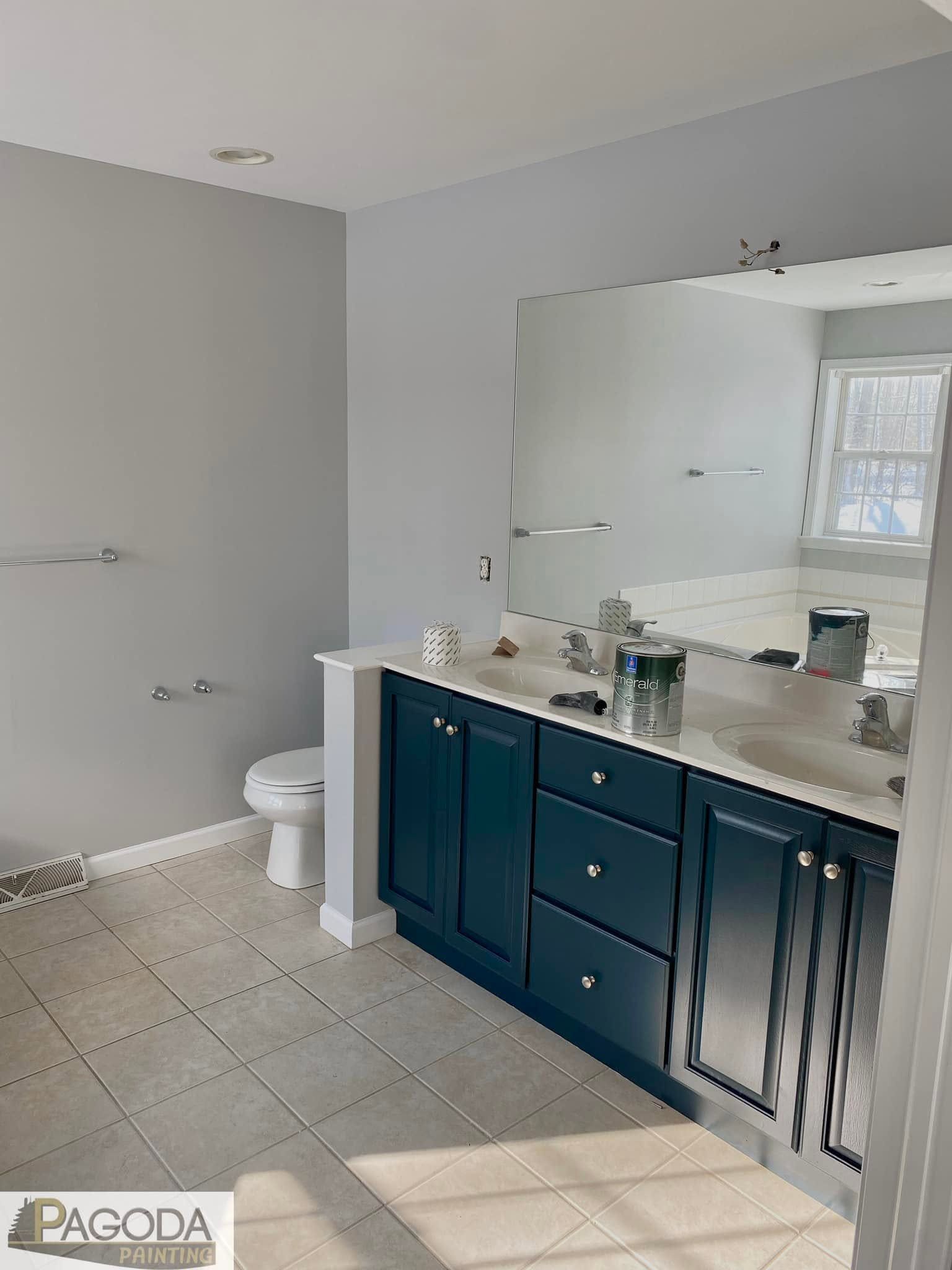 Bathroom with gray walls, tiled floor, white toilet, and dark blue vanity with mirror and double sink.
