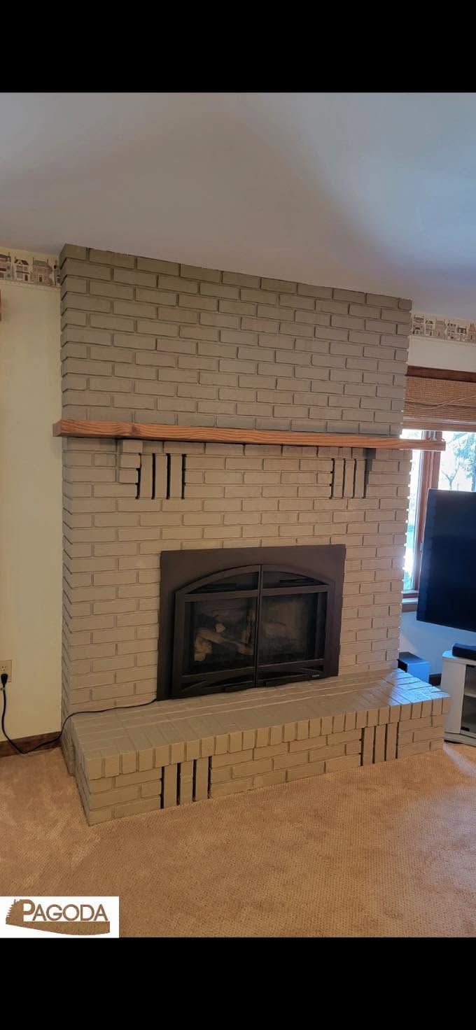 Brick fireplace with black insert and wooden mantel in a carpeted living room