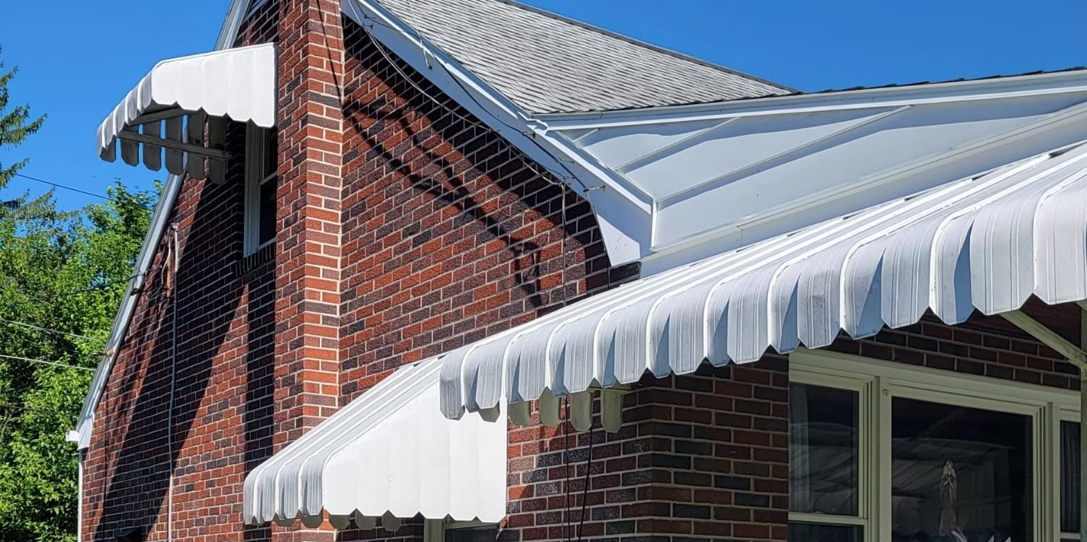 Brick house roof with white scalloped awnings and a small chimney against a blue sky