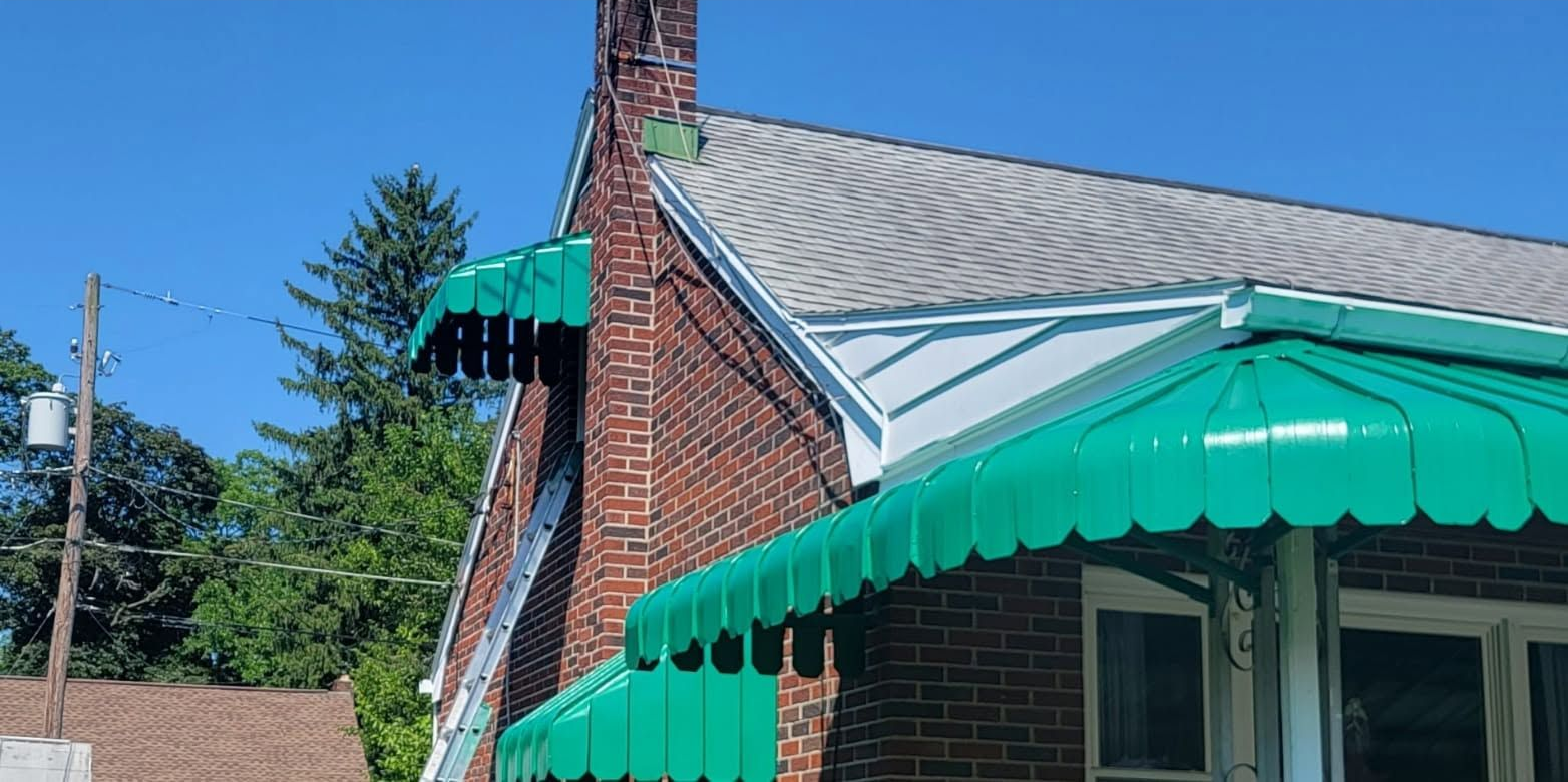 Brick house roof with green awnings and a chimney under a blue sky