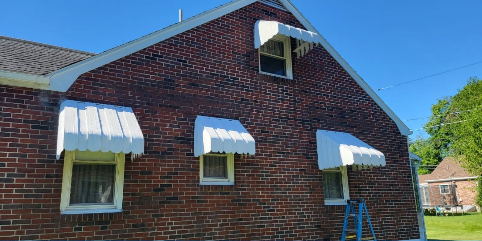 Brick house exterior with white awnings on windows and dormer under a blue sky
