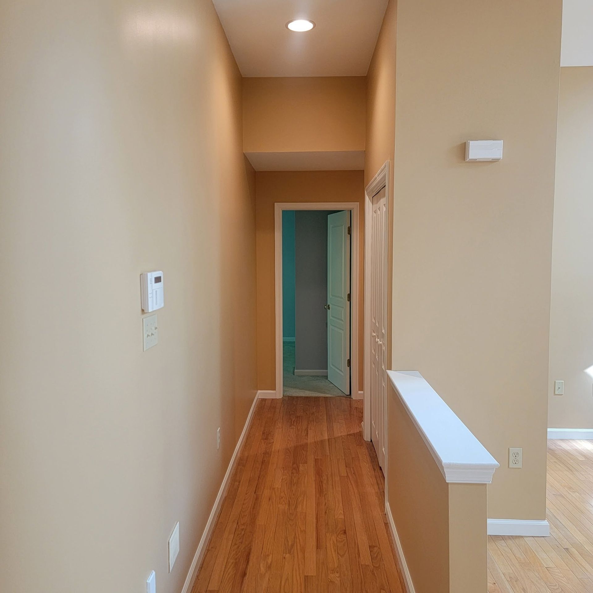 Narrow beige hallway with hardwood floor, white trim, and a doorway at the end.