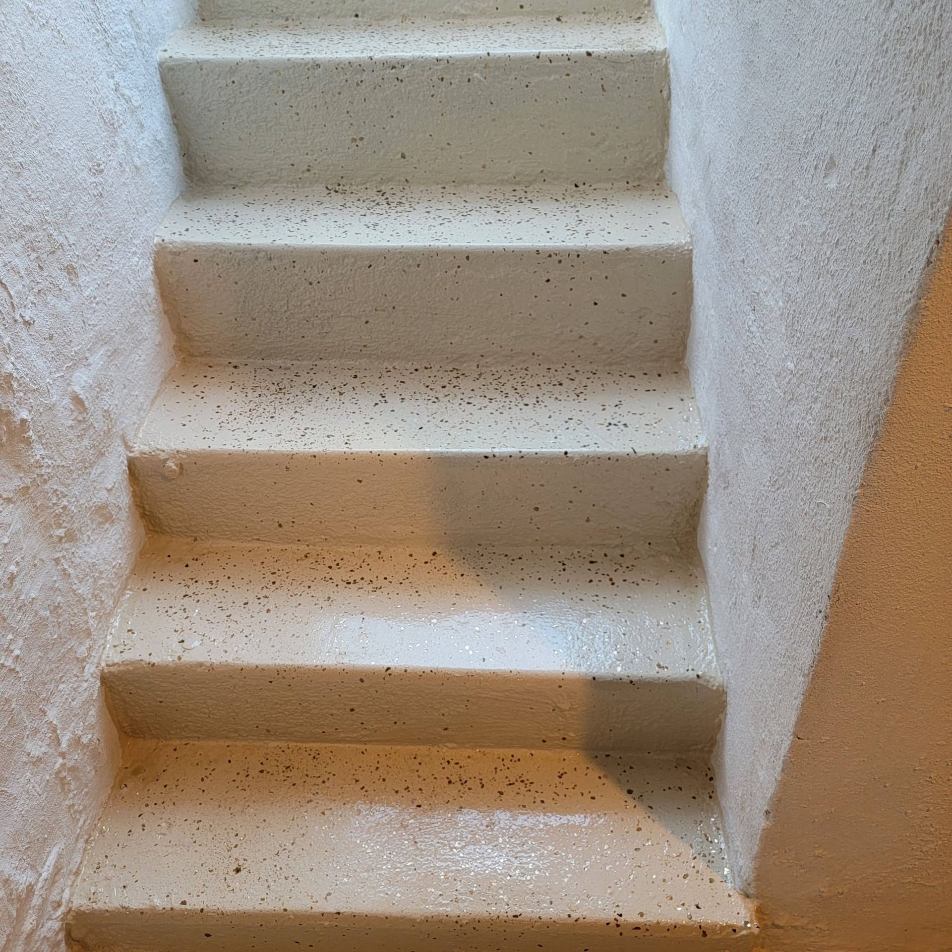 Steep indoor staircase with beige carpeted steps and white walls, viewed from below