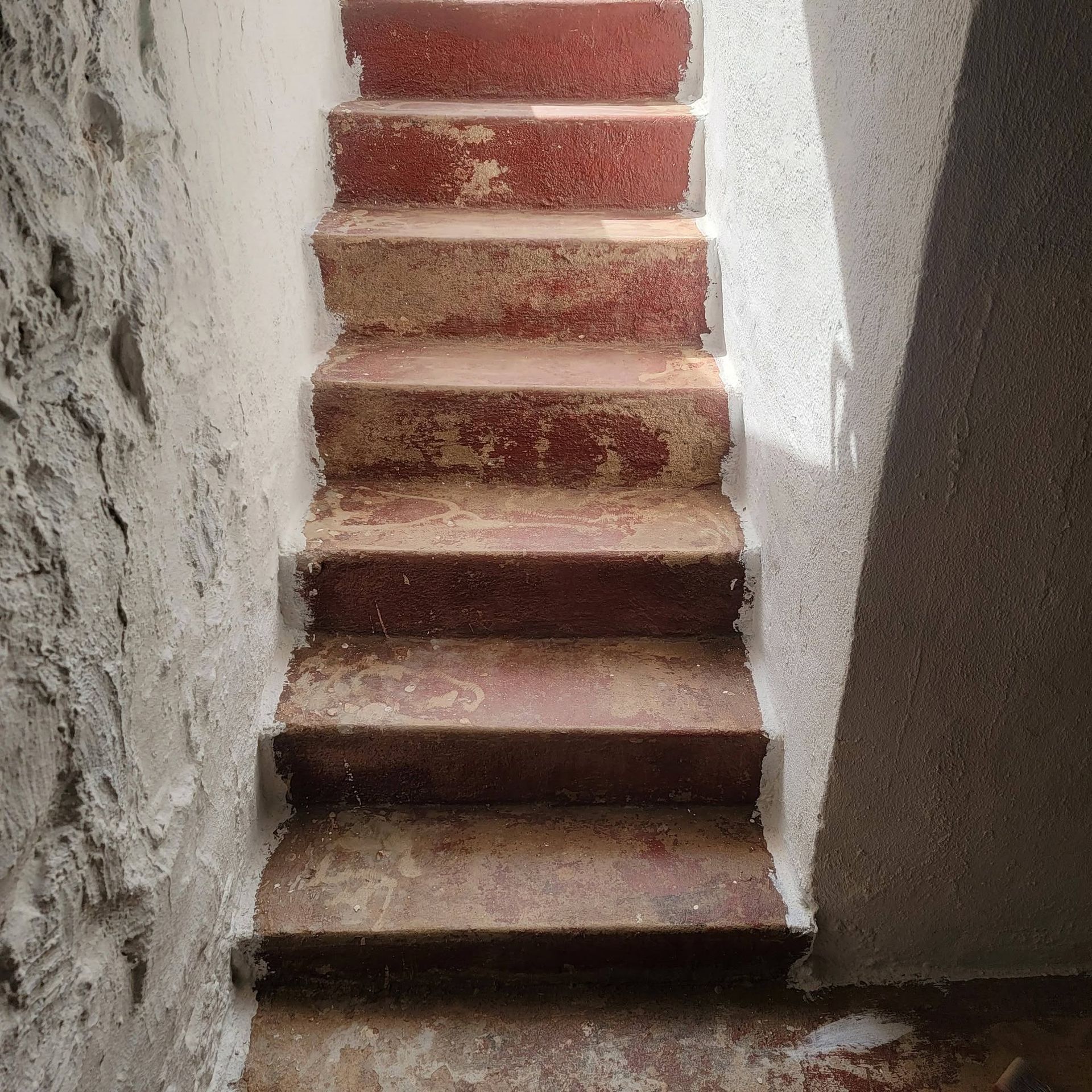 Narrow red-tiled staircase between rough stone walls, viewed from the bottom.