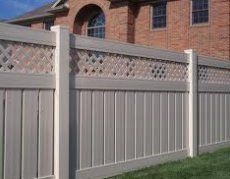 A white fence with a lattice design is in front of a brick house.