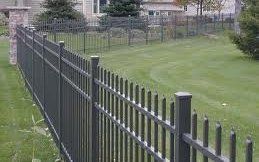 A black metal fence surrounds a lush green yard.