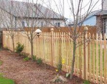 A wooden picket fence is surrounded by trees and bushes in front of a house.