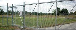 A chain link fence surrounds a baseball field in a park.